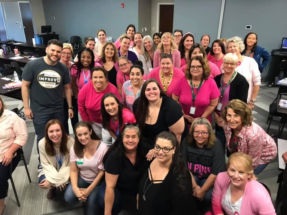 A large team posing for a group photo with an Improv U facilitator