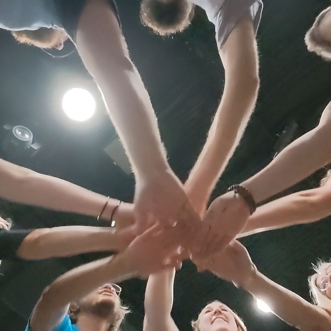 Hands stacked together in the center of a circle, seen from below